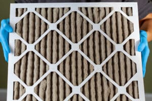 Gloved hands holding a dirty air filter.