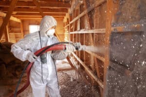 TRIO expert wearing a hazard suit and mask installing spray foam insulation in an attic.