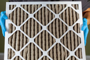 Gloved hands holding a dirty air filter.