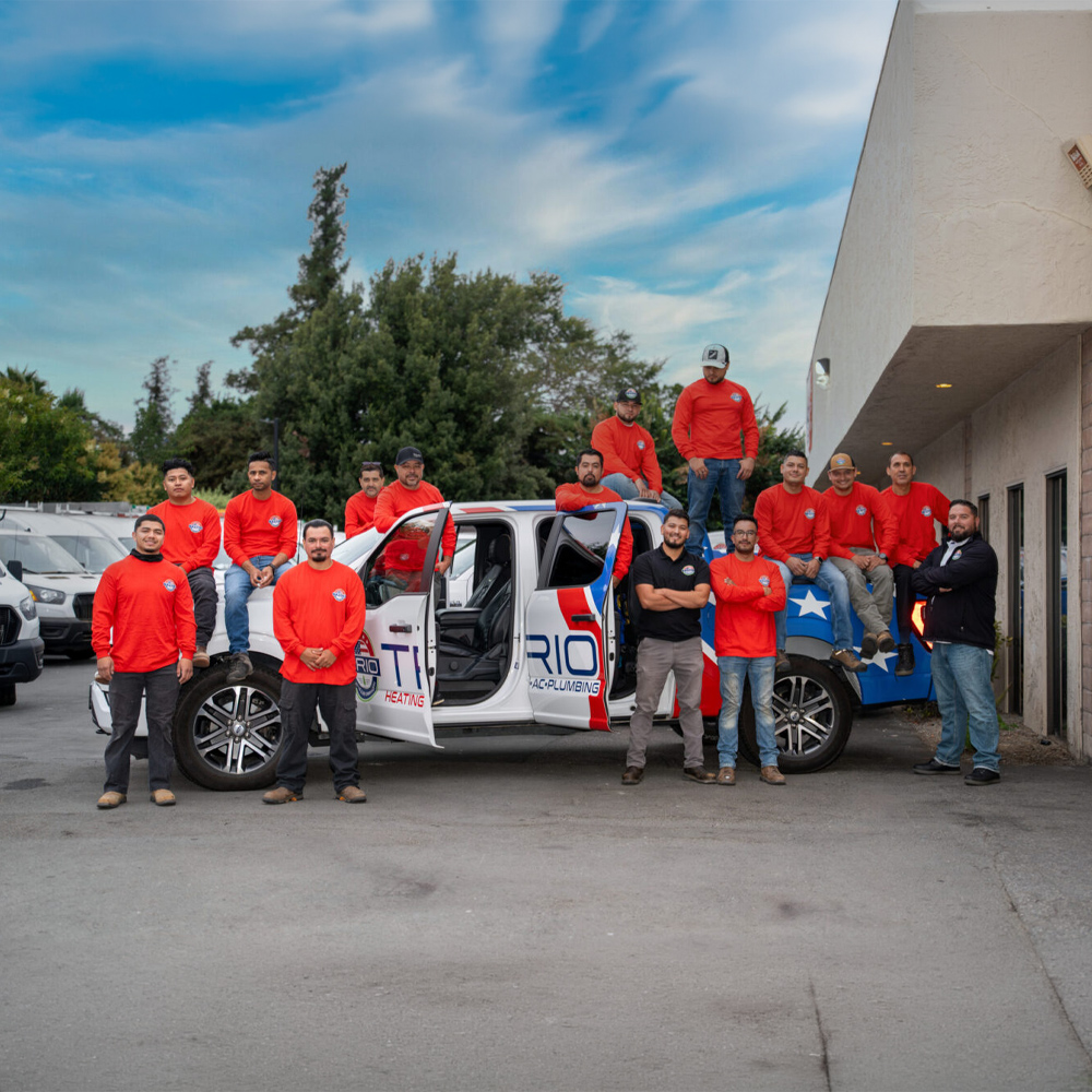 Team of workers in red uniforms posing by company truck with blue sky and greenery in the background.
