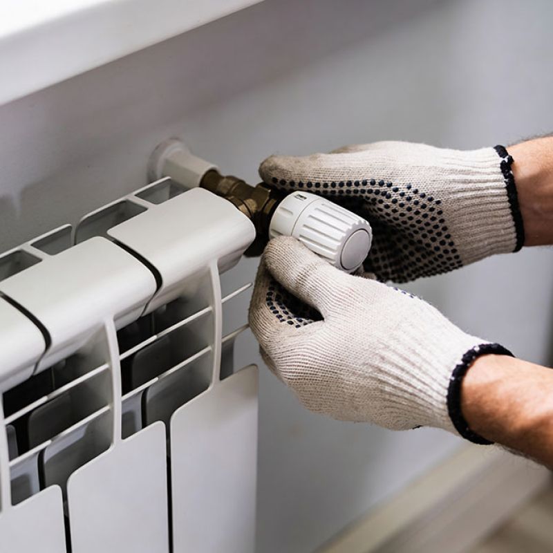 Hands adjusting radiator valve with gloves, close-up.
