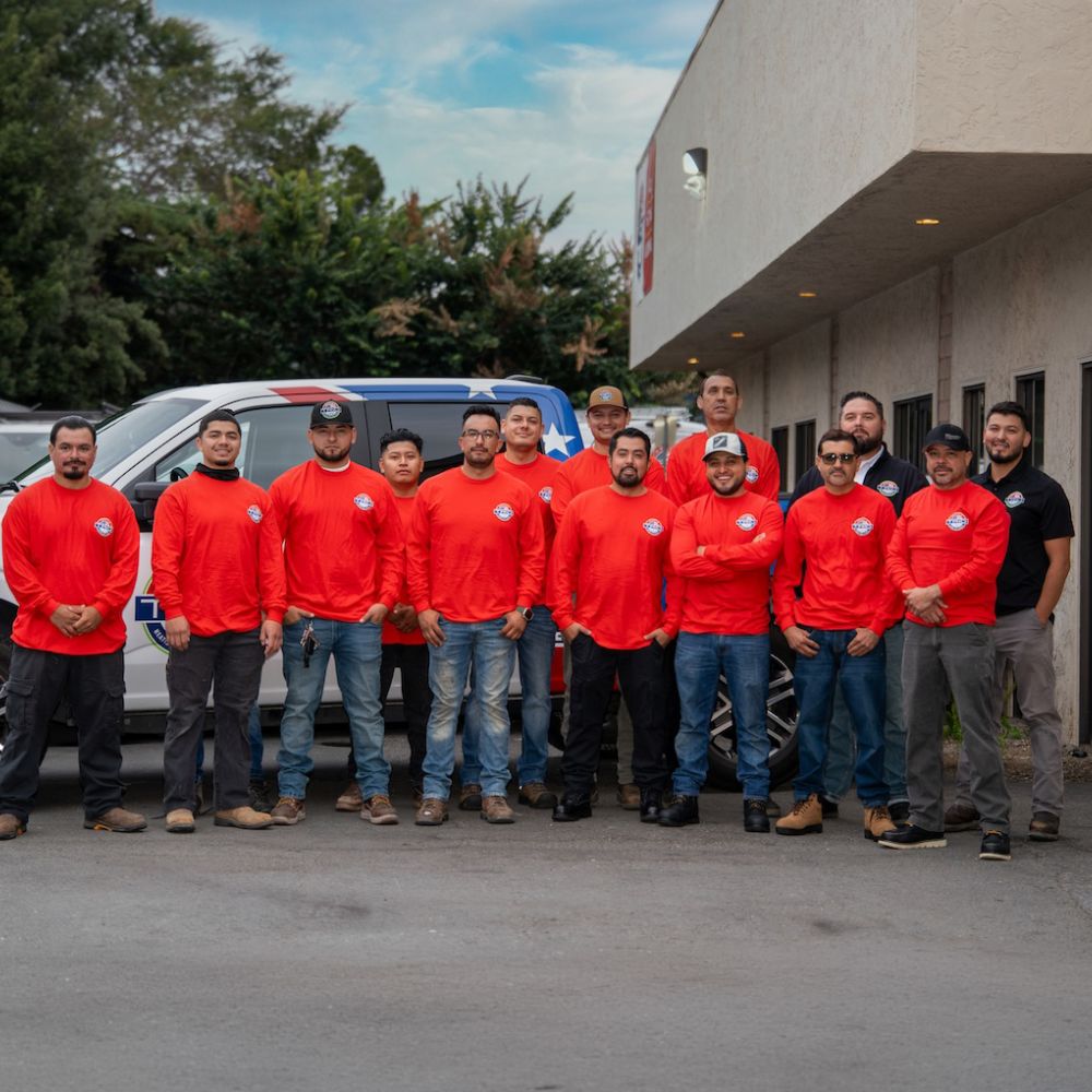 Team of workers in red shirts standing in front of a company vehicle outside a building.