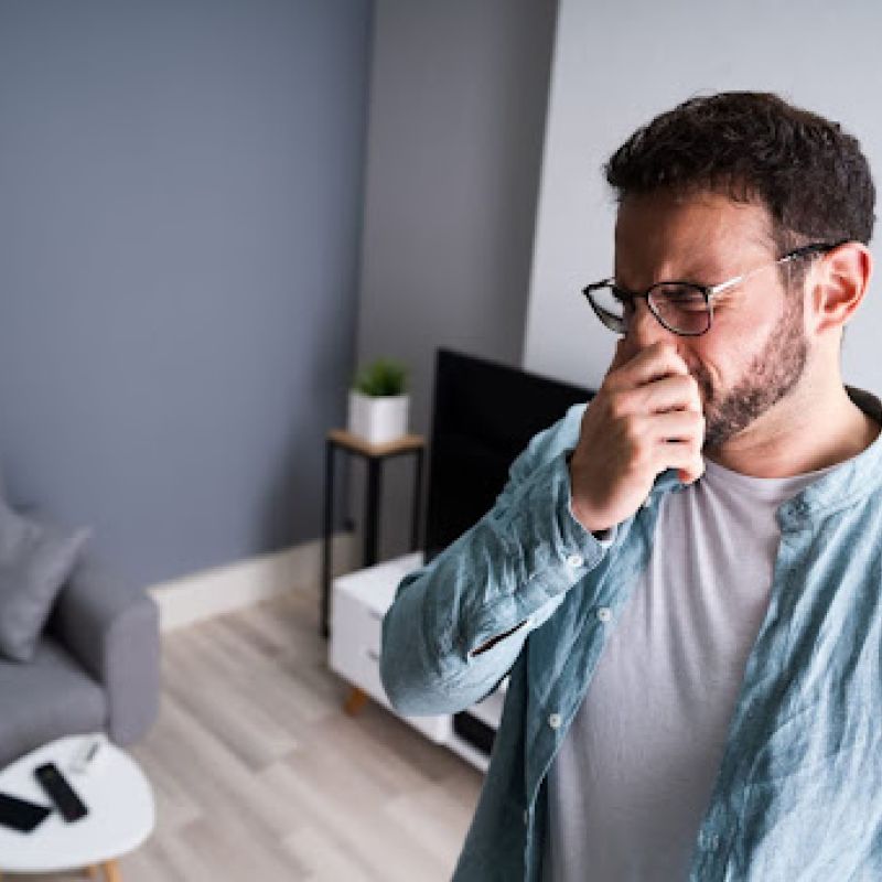 Man holding nose in his living room