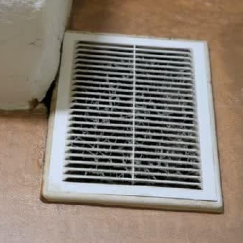 Dirty air vent on a brown floor near a wall corner, highlighting the need for cleaning and maintenance in home environments.
