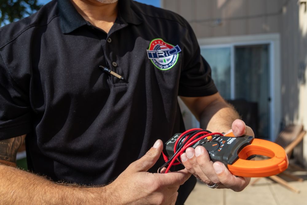 Technician holding a clamp meter in a black uniform outside.