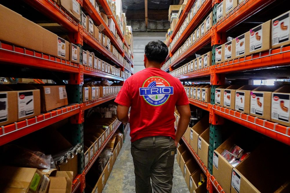 Warehouse worker in a red shirt navigating through organized shelves of boxes.