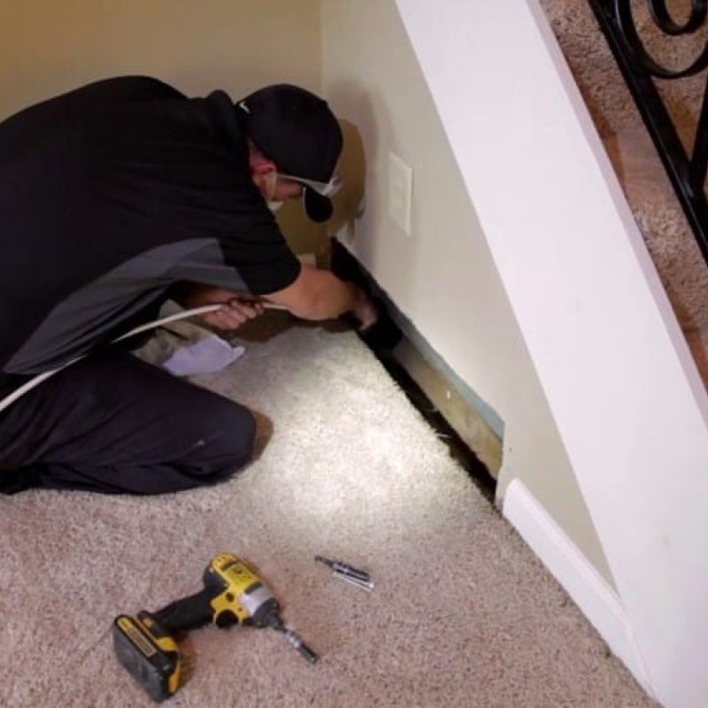 Technician cleaning HVAC duct under stairs with vacuum and tools on carpet.