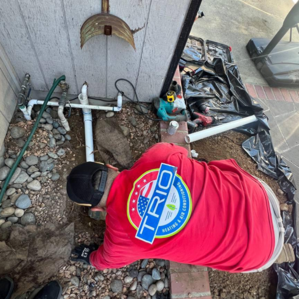 Technician in red shirt installing outdoor plumbing system with tools in a backyard setting.