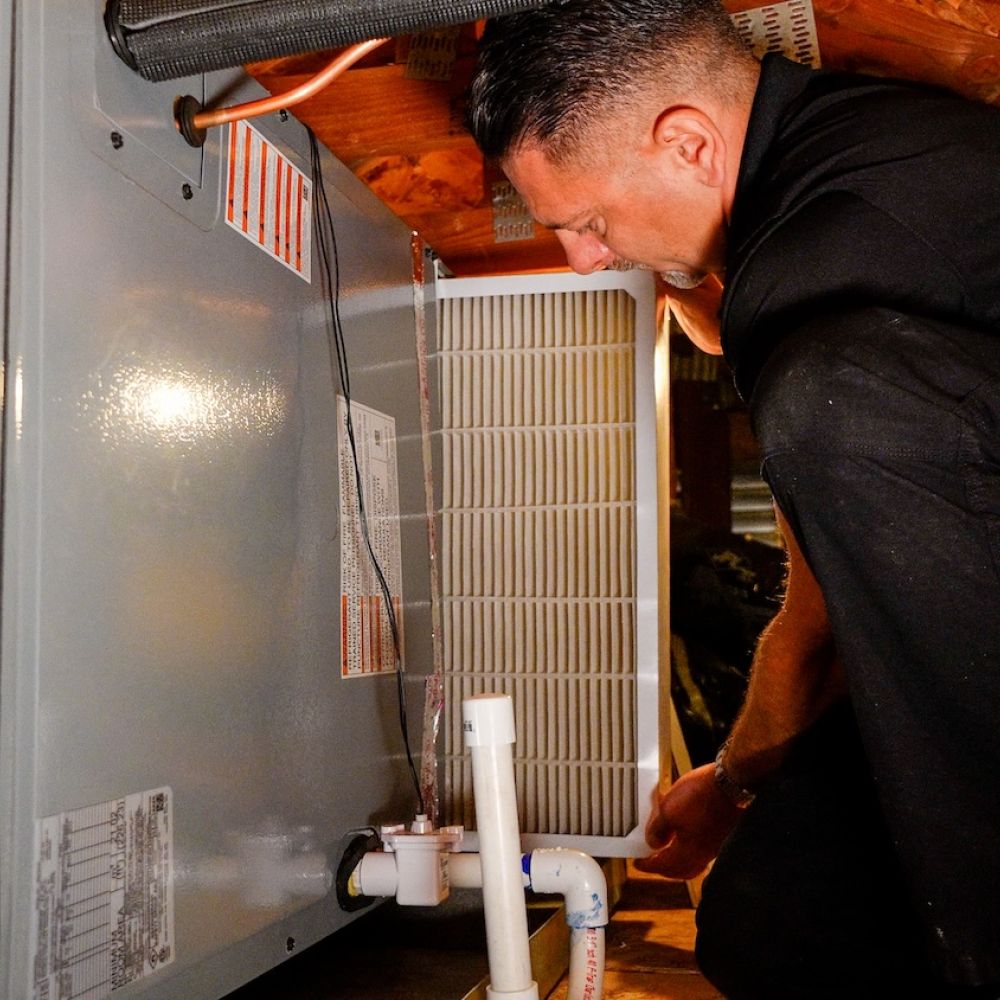 Technician performing routine HVAC maintenance in attic, replacing air filter for optimal heating and cooling efficiency.