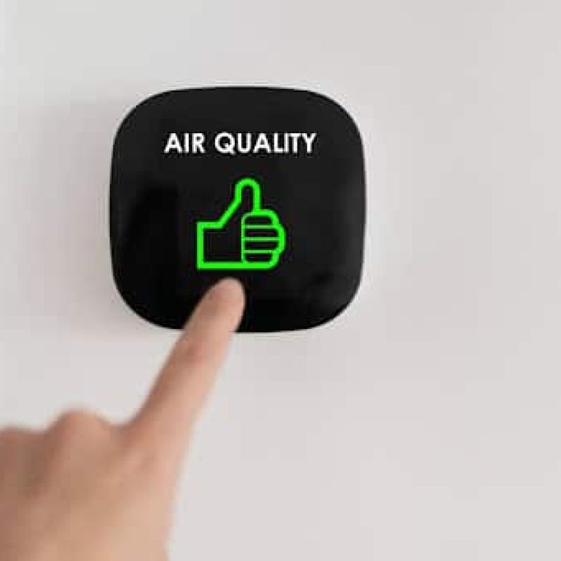 Homeowner touching air quality reader on wall.