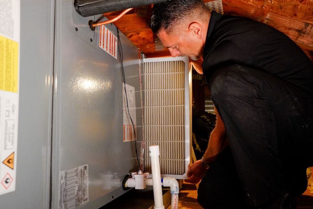 Technician performing routine HVAC maintenance in attic, replacing air filter for optimal heating and cooling efficiency.