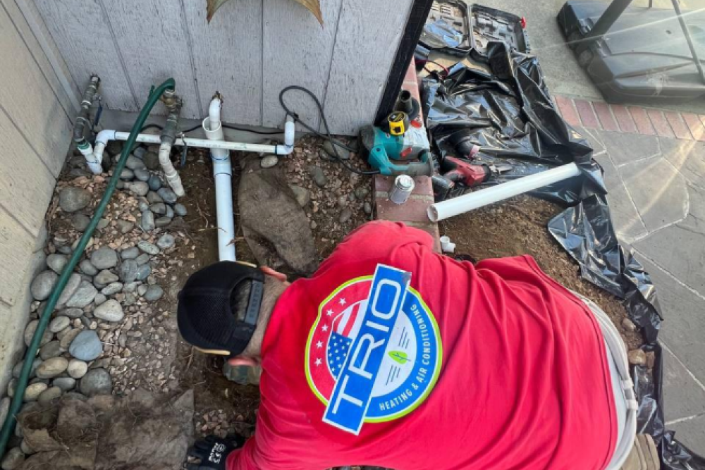 Technician in red shirt installing outdoor plumbing system with tools in a backyard setting.