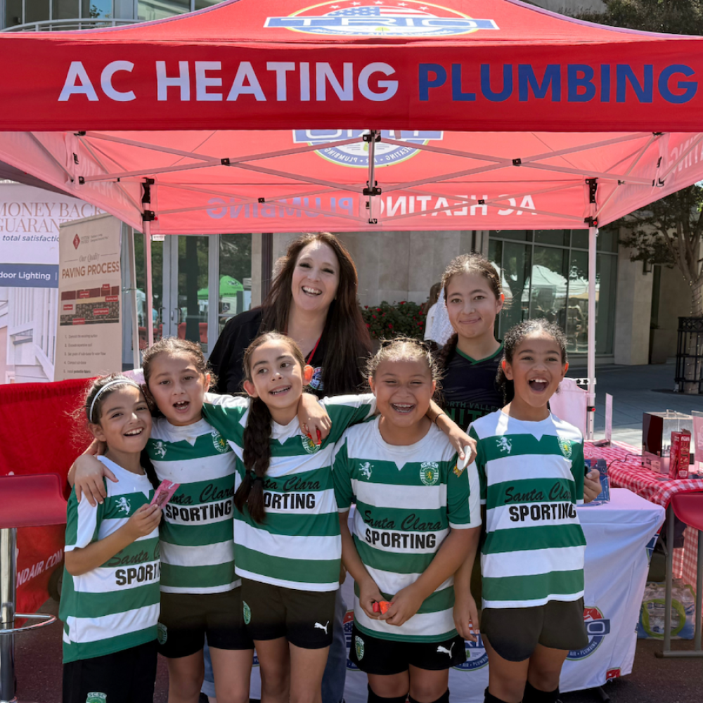 Youth soccer team posing under AC Heating Plumbing tent at outdoor event.
