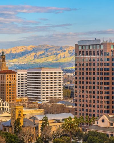 San Jose skyline with historic buildings and mountain backdrop under a blue sky.