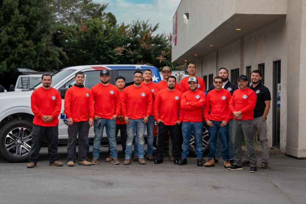 Team of workers in red shirts standing in front of a company vehicle outside a building.