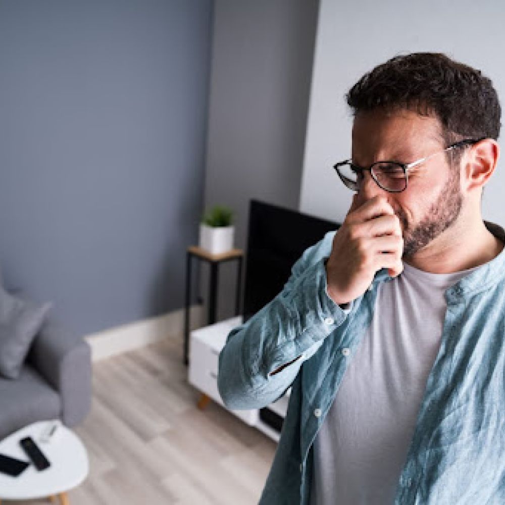 Man holding nose in his living room