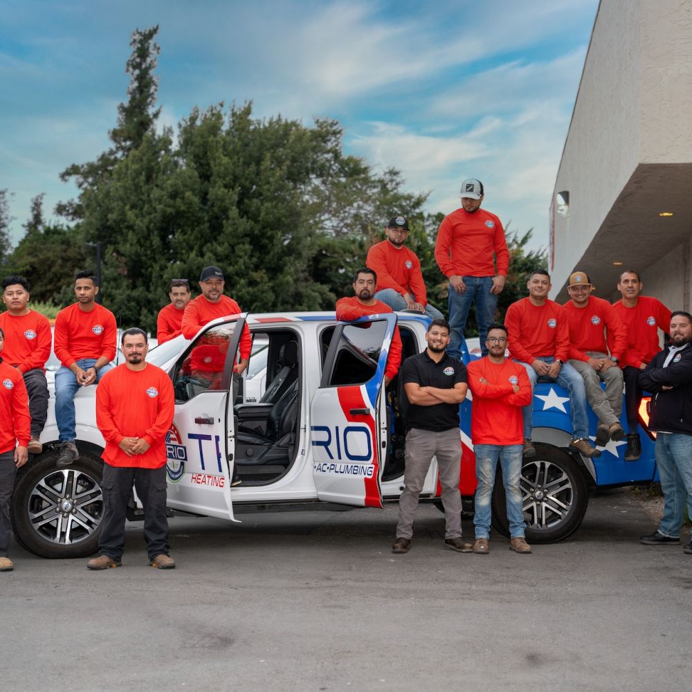 Team of workers in red shirts pose in front of a branded truck outside a building, showcasing company spirit and unity.