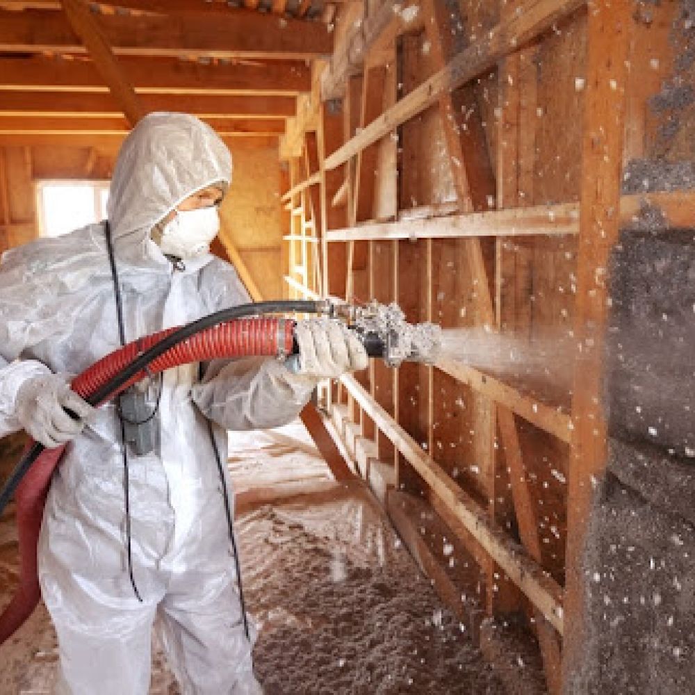 TRIO expert wearing a hazard suit and mask installing spray foam insulation in an attic.