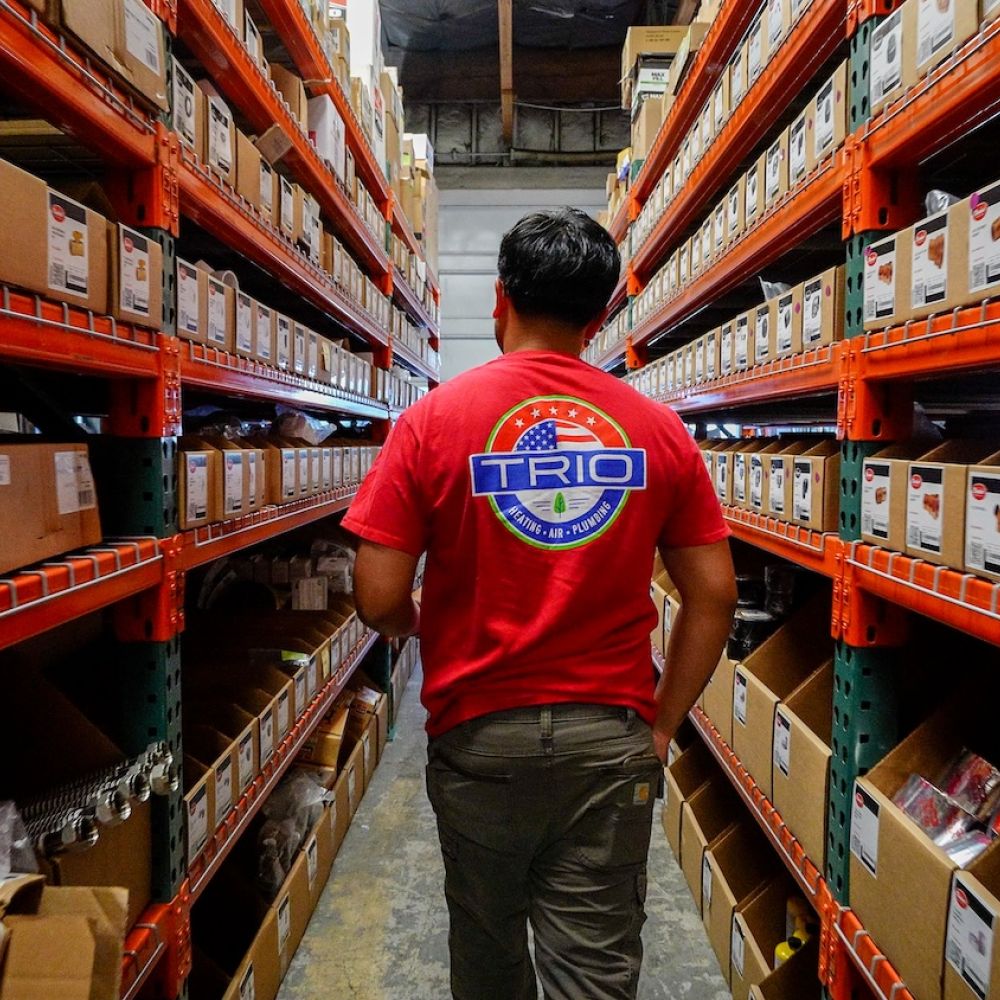 Warehouse worker in a red shirt navigating through organized shelves of boxes.