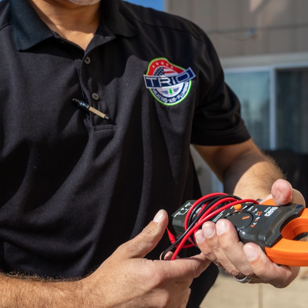 Technician holding a clamp meter in a black uniform outside.
