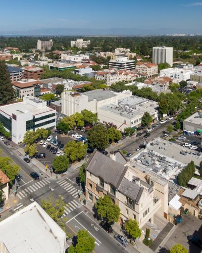 Aerial view of a city's downtown with buildings, streets, and greenery on a clear, sunny day.