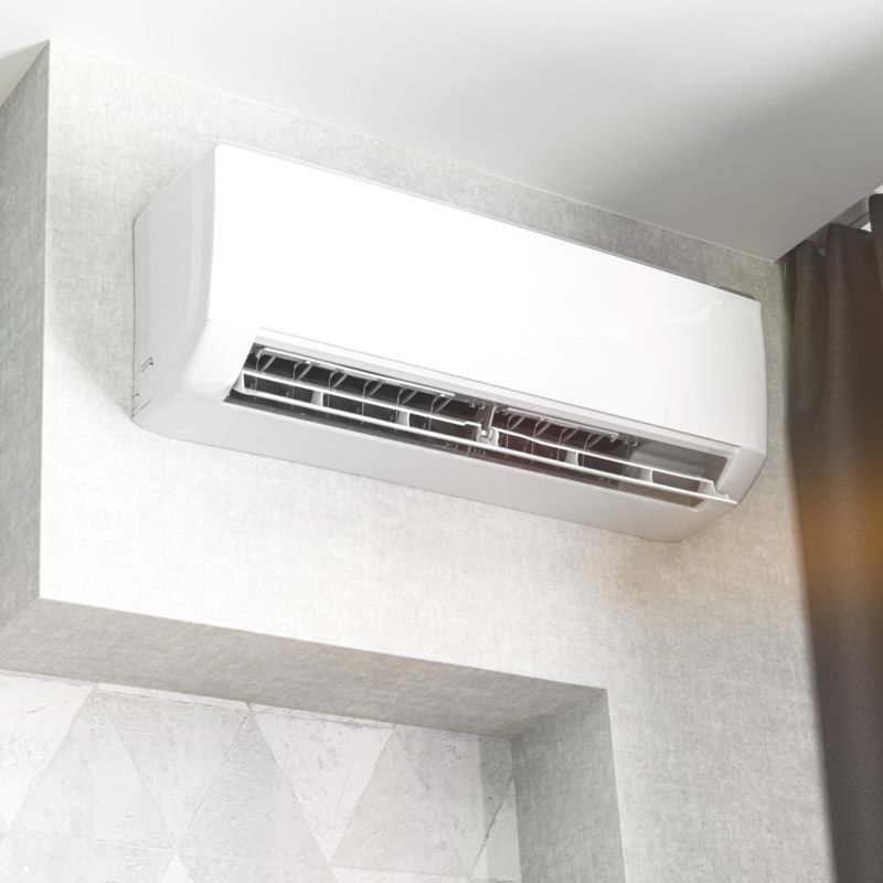 Wall-mounted air conditioner providing cool air in a modern room with gray textured walls and a dark curtain.